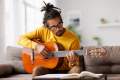 Man in a yellow sweater playing guitar on a couch