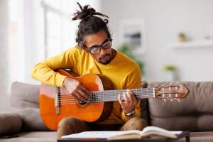 Man in a yellow sweater playing guitar on a couch