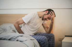 Sad man in pajamas cradles head in hand on bed