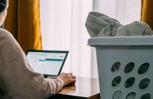 woman on laptop next to laundry basket