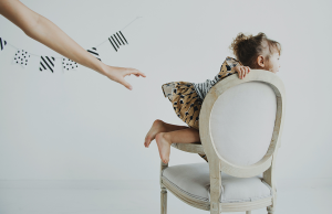 person reaching out hand to happy girl climbing on cushioned chair