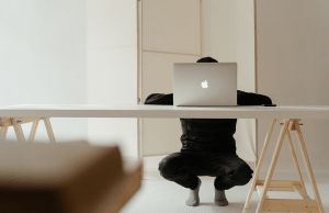 person squatting at large white table with silver MacBook