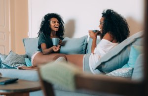 Happy young two black women sitting in the couch drinking coffee