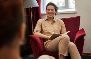 Happy overjoyed therapist making notes and looking at her female patient while laughing (JC) via Adobe Stock