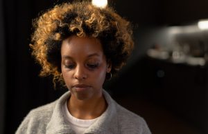 sad woman with black eye wearing a gray sweater in a black room