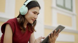 Woman in a red shirt looking at a tablet with headphones on