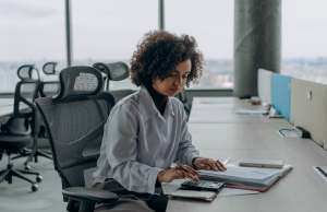 multi-racial woman in gray work clothes sitting at a desk while working