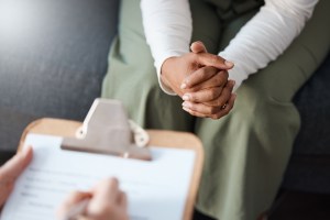 Woman's hands clasped waiting in front of a prescriber with a clipboard