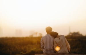 Man and woman sitting in a field at sunset