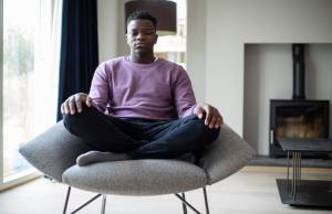 Black teenager in a purple shirt meditating in the living room