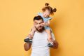 Father with his daughter on his shoulders while she pokes him in the eye