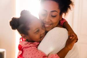 Mom in white hugging her child while smiling in sunlight