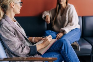 Professional therapist taking notes during therapy session with client on modern couch