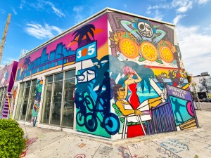 Colorful street art murals on building in Miami's Wynwood Walls district featuring vibrant geometric patterns, palm trees, and tropical imagery under blue sky