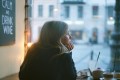 Woman sitting alone at a café window, chin resting on her hands, gazing outside in quiet reflection