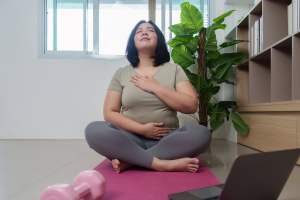 Woman doing breathing exercises sitting on a pink yoga mat