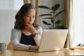 Middle-aged woman sitting at a table doing research on a laptop