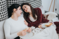 Two women sitting together on a bed, sharing food and talking closely, representing connection and intimacy in relationships