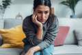Woman in a gray sweater zoning out, sitting on a gray couch