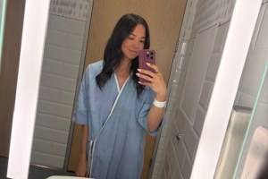 Emily Abbate wearing a blue hospital gown taking a selfie in the bathroom