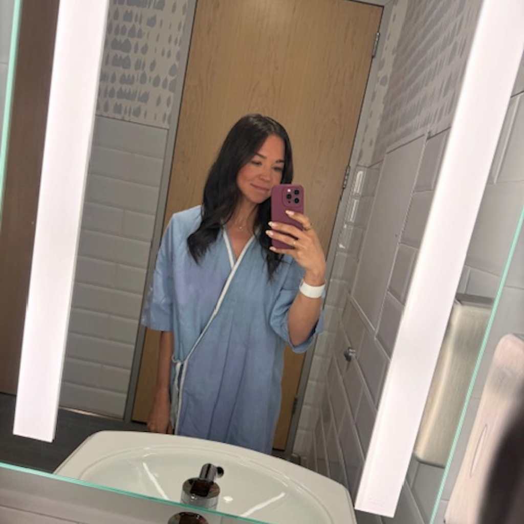 Brunette woman in a hospital gown taking a mirror selfie
