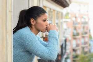 Woman in a blue sweater standing on a balcony looking over a rustic cityscape