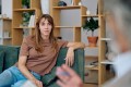 Woman sitting on a couch in a warm office setting, listening attentively during a conversation with a provider