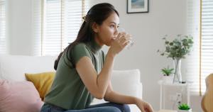 Woman in a green sweater on a white couch is taking medication with water