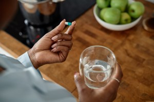 Woman's hand holding an antidepressant pill in one hand a cup of water in the other