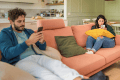 Young couple sitting on an orange couch far apart and looking at their phones
