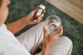 Person sitting looking at their prescription medication bottle with a glass of water in their other hand