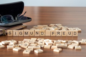 Sigmund Freud spelled out in Scrabble letters on a wood table, next to an old book and eye glasses