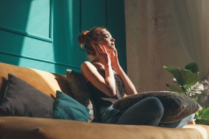 Woman sitting on sofa, home alone with face mask on, protecting her peace